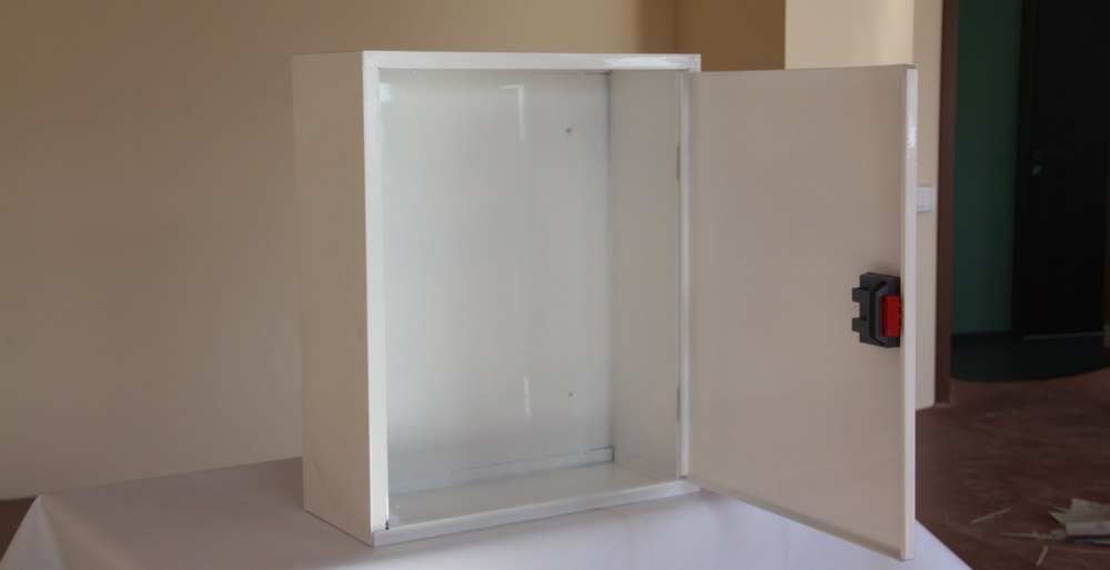 На столі із білим покриттям стоїть біла відкрита шафа пожежна квартирна в ній нічого не знаходиться. На фоні можна побачити квартирний антураж.