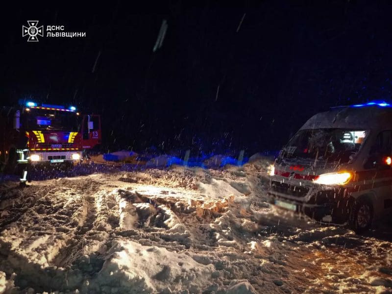 Пожарный автомобиль ГСЧС Волынской области буксирует белую машину скорой помощи из глубокого снежного сугроба днем.