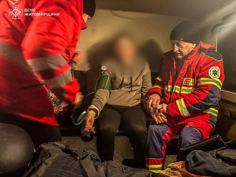 Врачи скорой помощи внутри автомобиля оказывают помощь пациенту, измеряя давление. Медики в красной профессиональной экипировке работают во время дежурства.