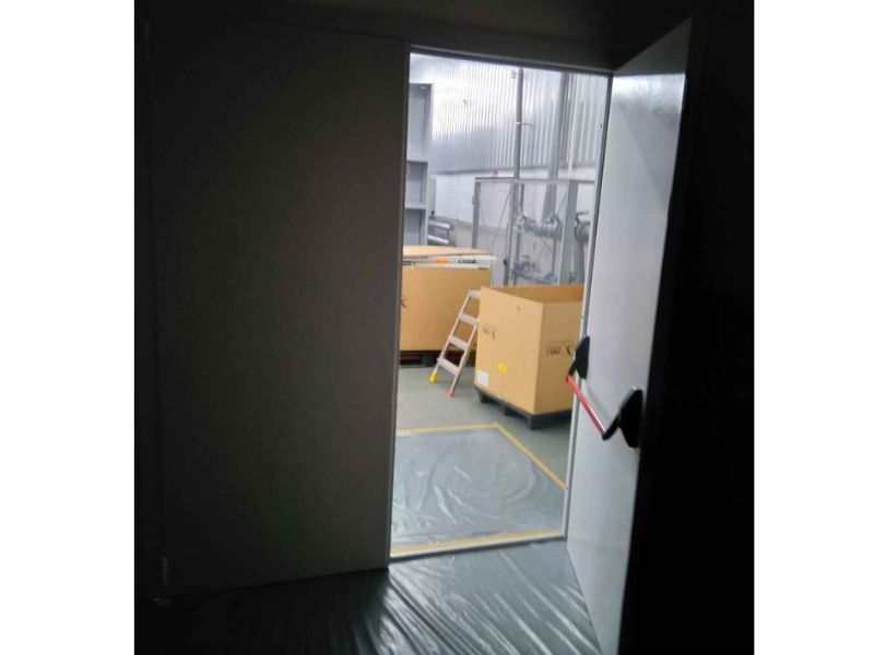 Відкриті вогнетривкі двері із системою антипаніка із червоним поручнем, у пройомі відкритих дверей видно велике пусте складське приміщення