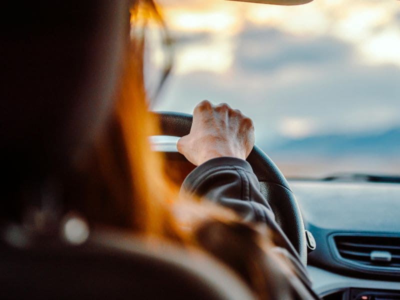 На фото видно руль та жіночі руки, машина рухається вперед