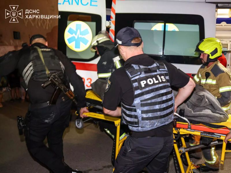 Рятувальники ДСНС та співробітники поліції транспортують врятовану жінку на ношах до карети швидкої допомоги.