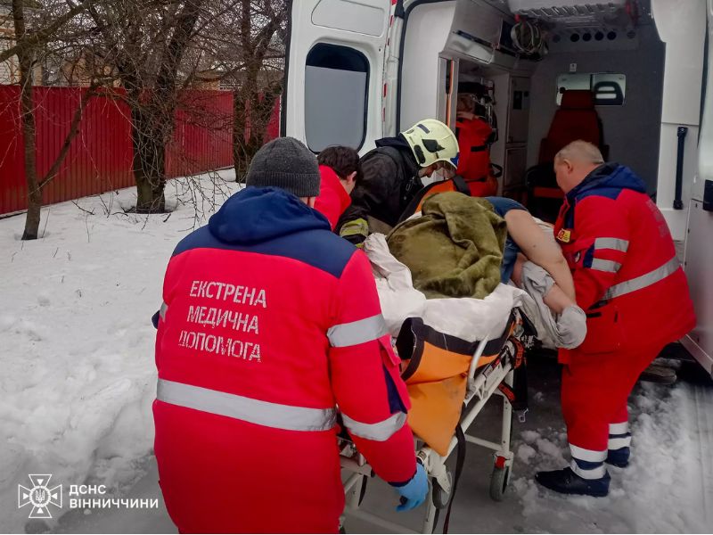 Рятувальники ДСНС та медики екстреної допомоги транспортують постраждалу особу на ношах до карети швидкої допомоги на засніженій вулиці Вінниччини.