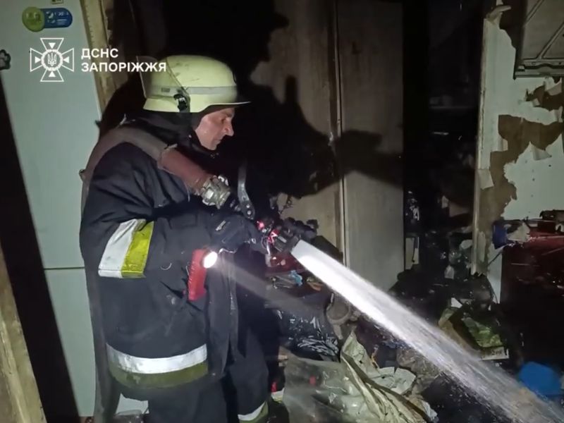 Співробітник ДСНС ліквідує пожежу в житловій багатоповерхівці Запоріжжя за допомогою водяного ствола.