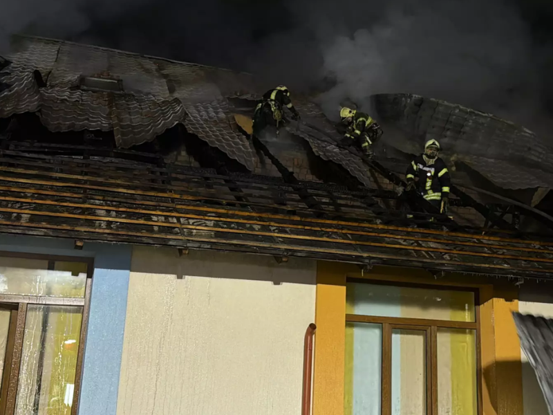 Вогнеборці у захисній формі та касках працюють на даху будівлі вночі. Рятувальники розбирають обгорілу покрівлю, з-під якої йде дим, використовуючи ліхтарі для освітлення місця робіт.