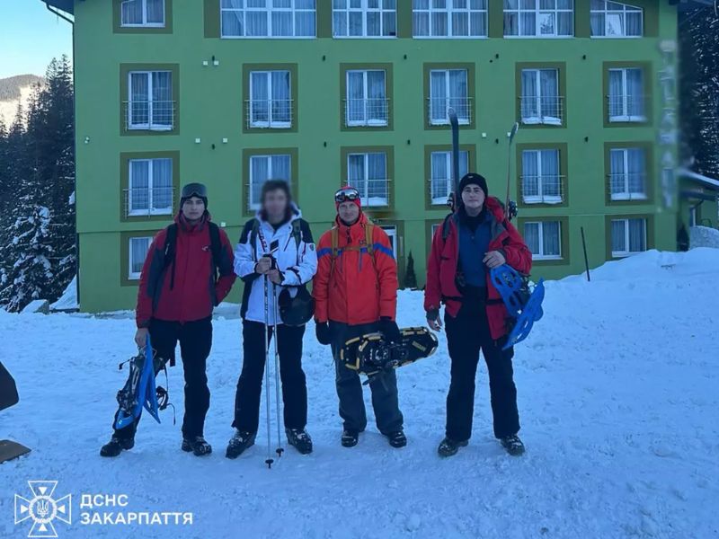 Группа горноспасателей ГСЧС Закарпатья в зимней экипировке со снегоступами и лыжными палками на фоне зеленого здания в горах.