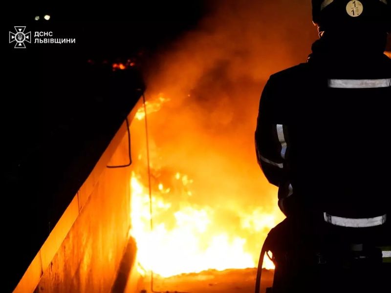 Пожарный ГСЧС Львовской области на фоне сильного пламени во время ликвидации ночного пожара, силуэт спасателя в экипировке с отражателями.