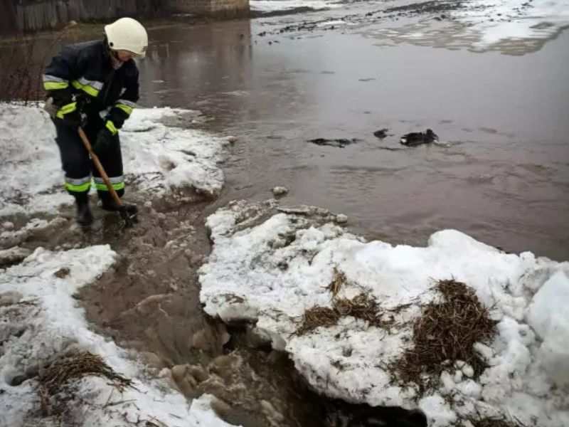 Сотрудник ГСЧС лопатой расчищает русло для отвода талой воды, борьба с подтоплением из-за таяния снега и льда у реки.