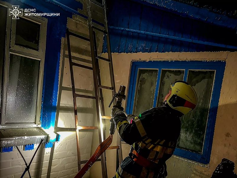 Пожарный ГСЧС Житомирской области с пожарным стволом и лестницей ликвидирует возгорание в частном доме в ночное время.
