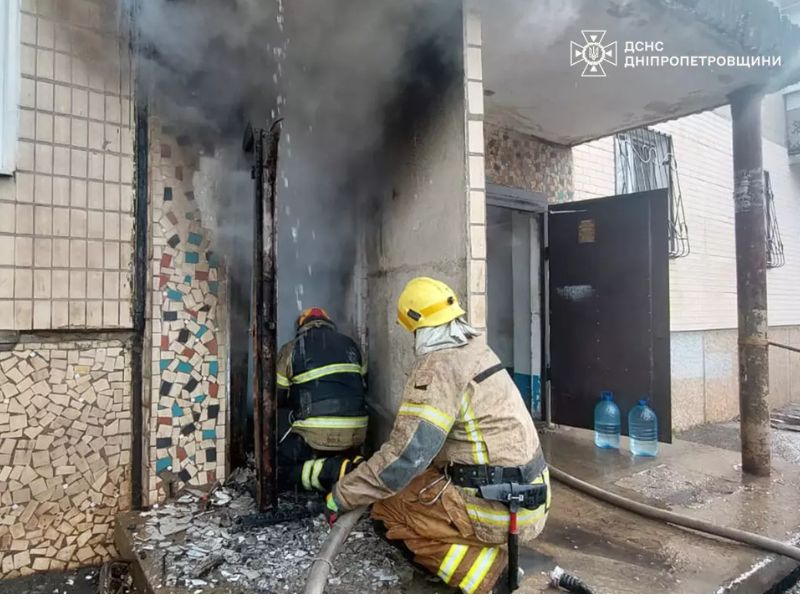 Пожарные ГСЧС Днепропетровской области тушат огонь в подъезде жилого дома, густой дым из дверного проема, спасатели в шлемах и защитной форме с пожарным шлангом.