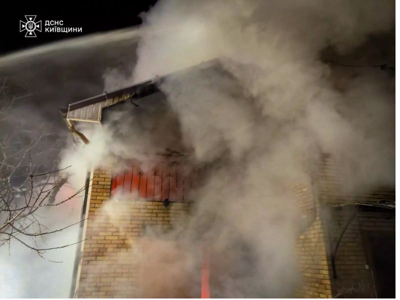 Пожарные ГСЧС тушат огонь в частном кирпичном доме в Киевской области, густой дым валит из-под крыши здания ночью.