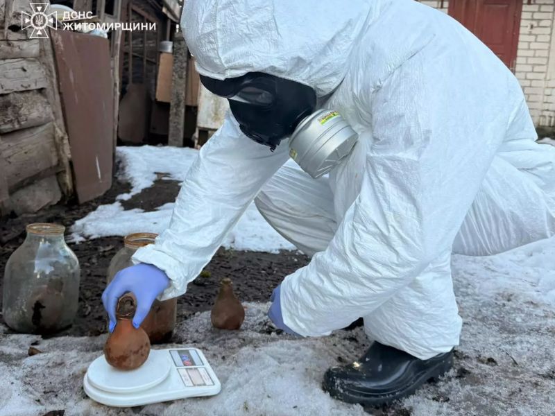 Фахівець ДСНС у білому захисному костюмі та протигазі зважує ємності з ртуттю на електронних вагах на фоні снігу в Житомирській області під час ліквідації хімічної загрози.