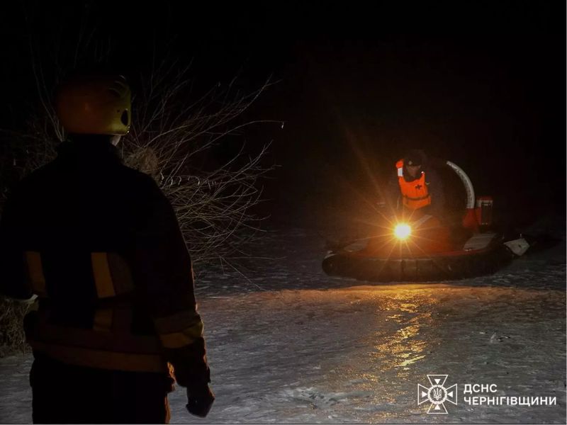 Вид со спины спасателя в желтом шлеме на приближающееся красное судно на воздушной подушке с включенным ярким прожектором на льду ночью.