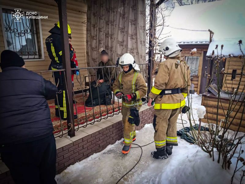 Сотрудники ГСЧС Киевской области оказывают помощь мужчине на веранде дома после спасательной операции зимой.