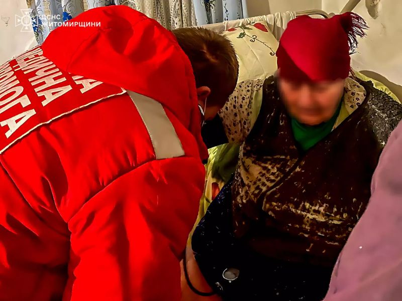 Медицинский работник в красной куртке оказывает экстренную помощь пожилой женщине в домашней обстановке после пожара.