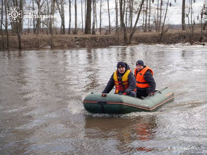 Двое спасателей ГСЧС в спасательных жилетах патрулируют реку на надувной моторной лодке в Полтавской области.
