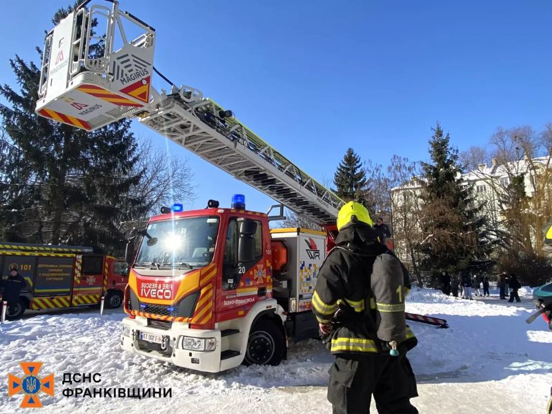 Пожарный автомобиль Iveco с выдвижной лестницей Magirus на фоне заснеженных деревьев в Ивано-Франковске. Спасатель в защитном снаряжении стоит спиной к камере.