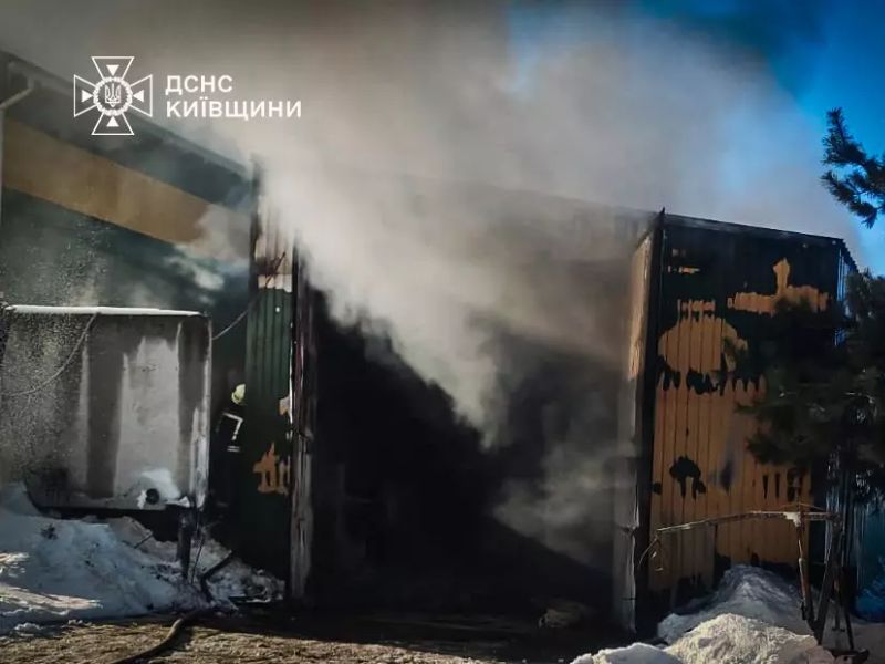 Густой дым валит из открытых дверей горящего металлического склада в Киевской области во время работы пожарных расчетов ГСЧС зимой.