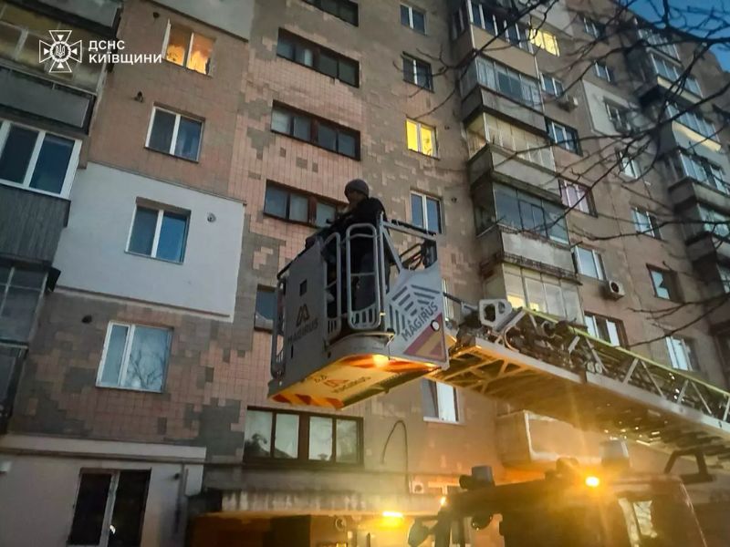Рятувальники ДСНС Київської області здійснюють гасіння пожежі в багатоповерхівці. Пожежна автодрабина Magirus розгорнута до вікна квартири, де видно відкрите полум'я, у люльці працює вогнеборець.