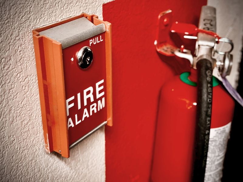 На фоні білої стіни знаходиться пожежна сигналізація, вогнегасник