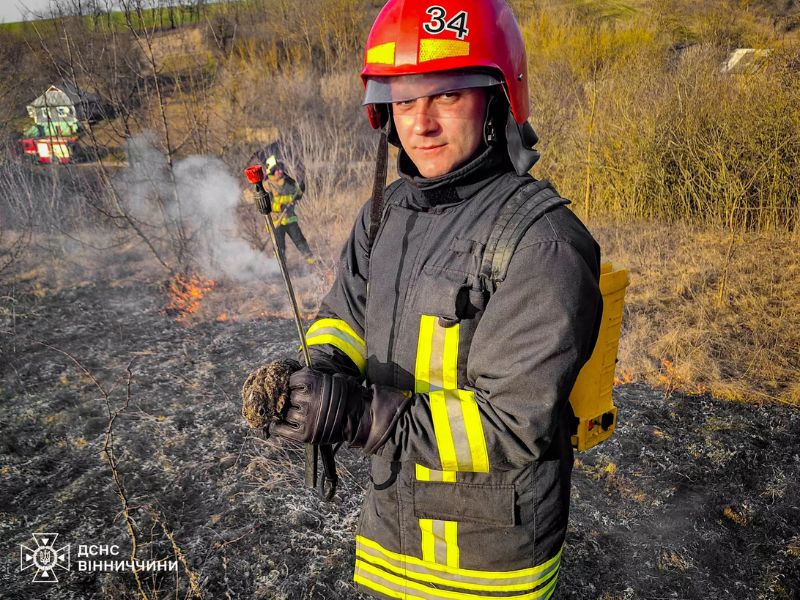 Пожежник ДСНС Вінниччини зі спецспорядженням та врятованим зайченям на фоні ліквідації загоряння сухої трави.
