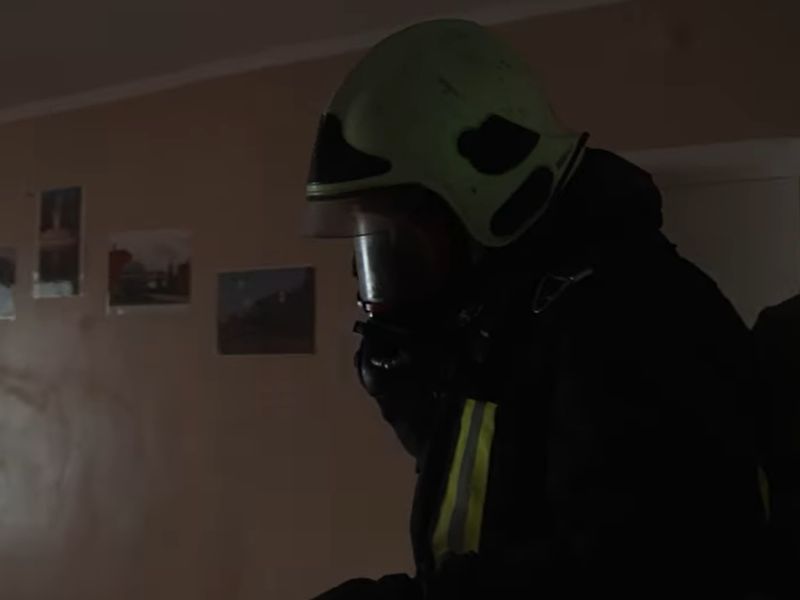 Пожарный ГСЧС в защитном шлеме и дыхательном аппарате проводит разведку в задымленной квартире во время ликвидации пожара.