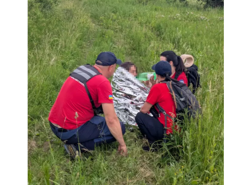 Співробітники ДСНС надають першу допомогу знайденій людині в полі, вкривши її рятувальною термоковдрою.