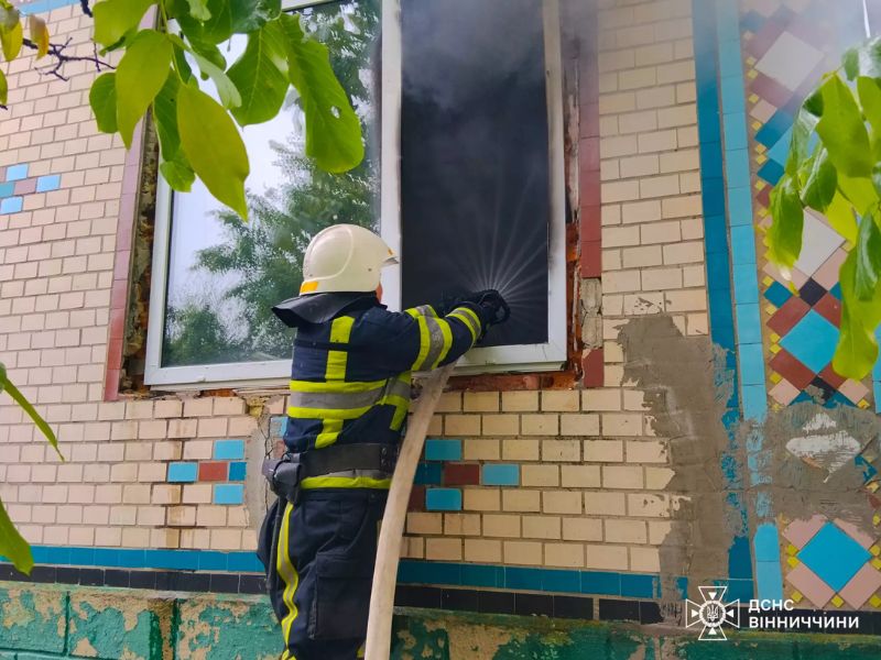 Співробітник ДСНС Вінниччини ліквідує пожежу через вікно задимленої цегляної будівлі.