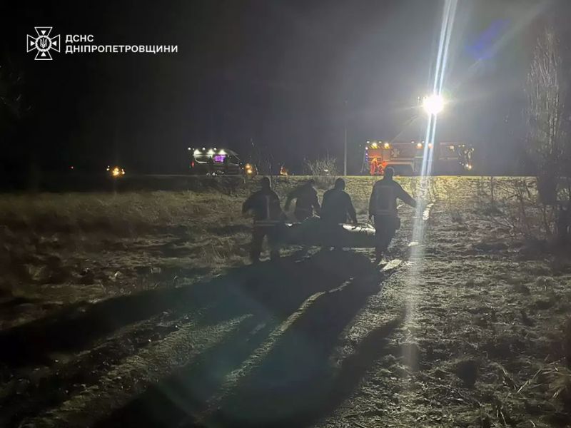 Спасатели ГСЧС Днепропетровской области работают ночью на месте происшествия. Группа сотрудников в форме переносит оборудование на фоне пожарной машины с ярким освещением.