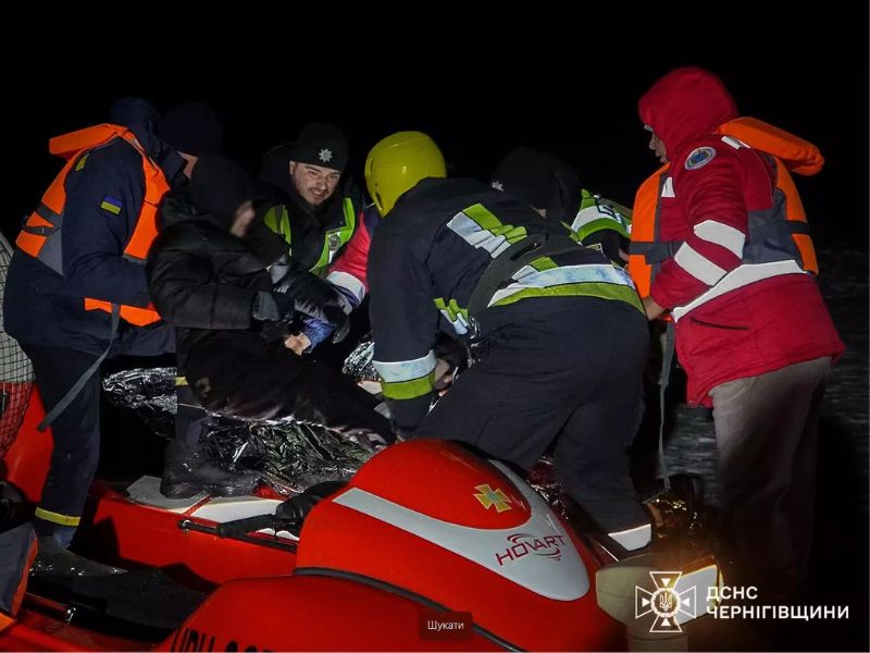 Спасатели ГСЧС и полиция оказывают помощь человеку, завернутому в термоодеяло, на борту красного спасательного катера Hovart ночью.