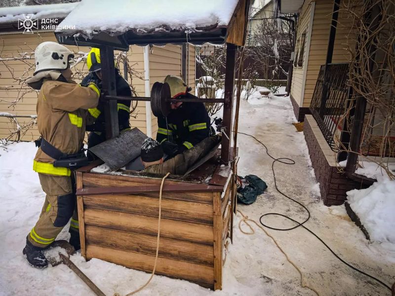 Спасатели ГСЧС Киевской области вытаскивают человека из деревянного колодца зимой с помощью спасательных веревок.