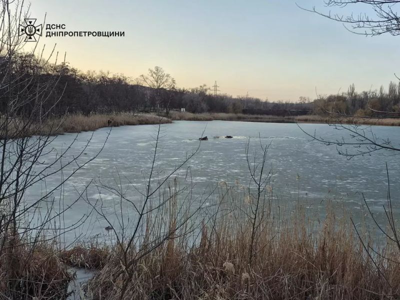 Вид на замерзшее озеро с сухим камышом на переднем плане и темными промоинами на тонком льду. В верхнем левом углу логотип ГСЧС Днепропетровской области. Сцена иллюстрирует опасность выхода на лед весной.