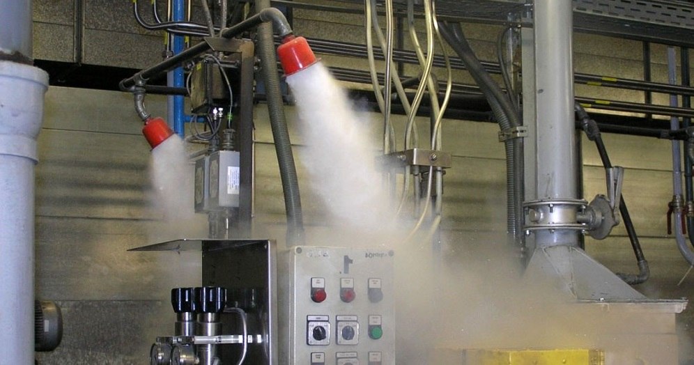 На фото виробничий цех в кому знаходиться різне обладнання серед якого також є установка автоматичного самостійного гасіння, що є активована. У цього приміщення сірі стіни та труби, великі металеві витяжки та труби.