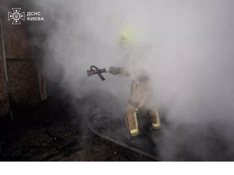 Рятувальник ДСНС Києва направляє пожежний ствол на осередок горіння в умовах нульової видимості через густий білий дим.