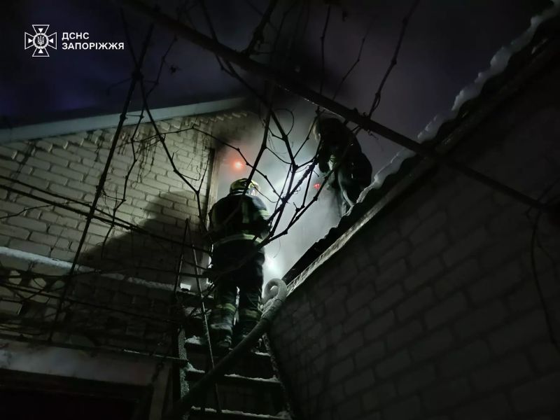 Вогнеборці ДСНС Запоріжжя на пожежній драбині під час гасіння приватного будинку вночі. Рятувальники працюють біля засніженого даху будівлі в складних умовах.
