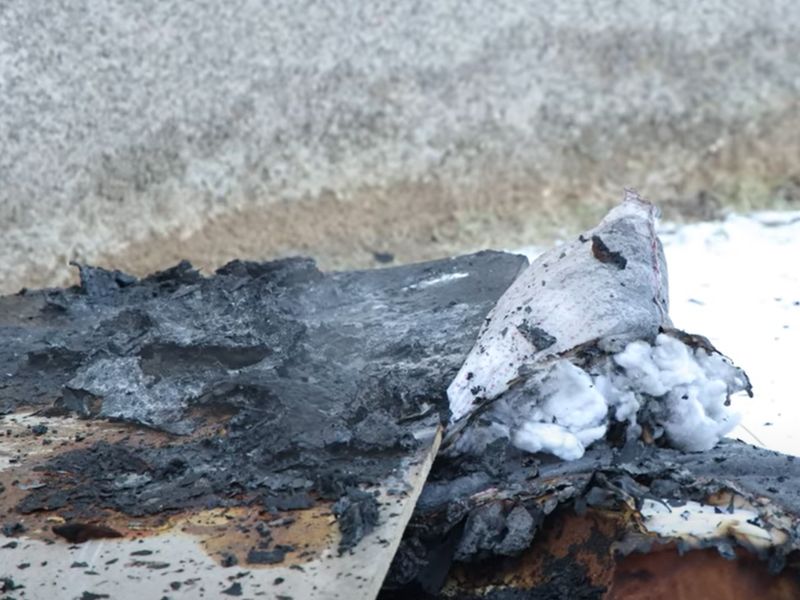 Крупный план обгоревших остатков домашних вещей и мебели на снегу после ликвидации пожара в жилом доме.